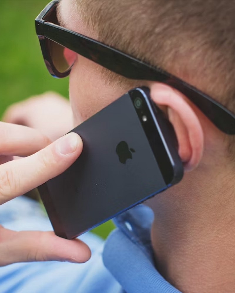 Person wearing sunglasses and holding a black smartphone with an Apple logo.